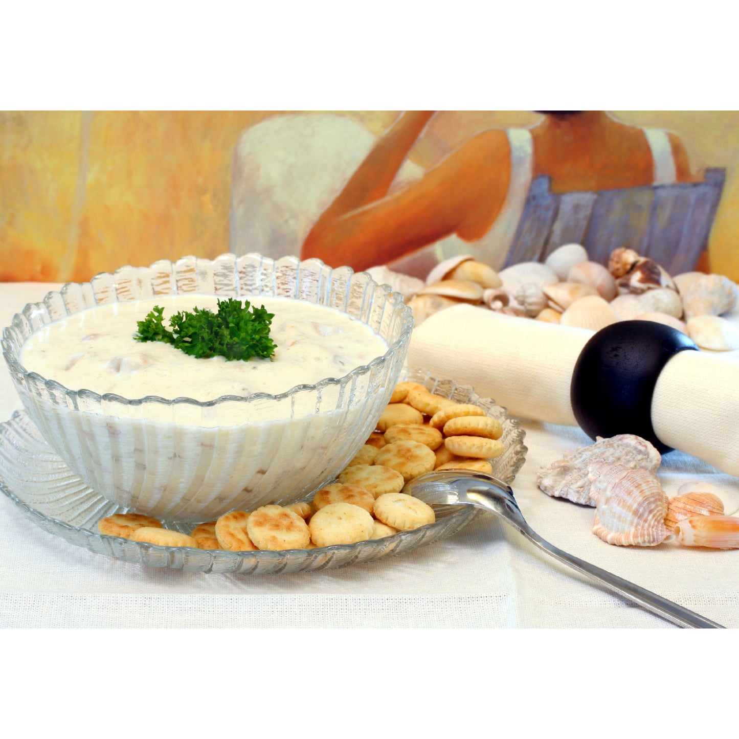 Bowl of creamy clam chowder garnished with parsley, served with Westminster oyster crackers on a glass plate, with seashell decor in the background.