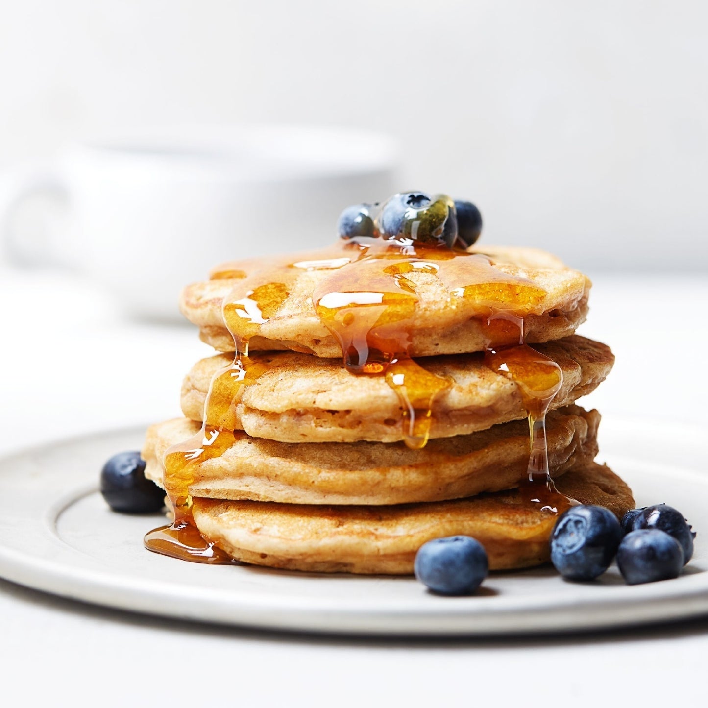 Stack of golden pancakes topped with syrup and fresh blueberries on a white plate.